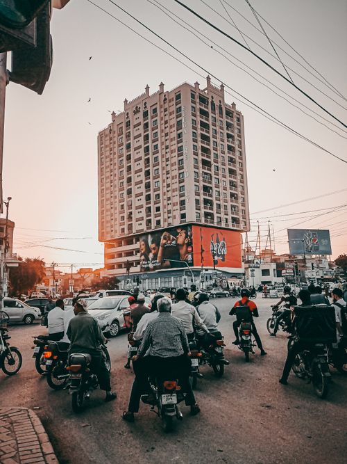 Free Motorcycles line up at a bustling city intersection with high-rise building in view. Stock Photo