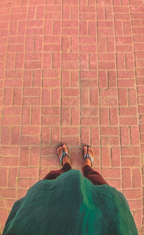 A Person Wearing Slippers while Standing on a Brown Brick Floor