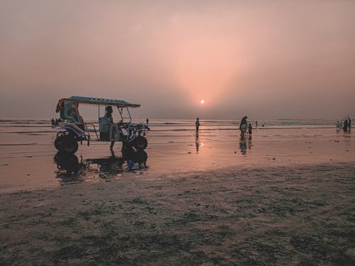 A Man Driving an Auto Rickshaw on the Seashore at Sunset