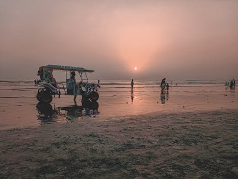 A scenic view of an auto rickshaw on a beach during sunset, with people in the background.