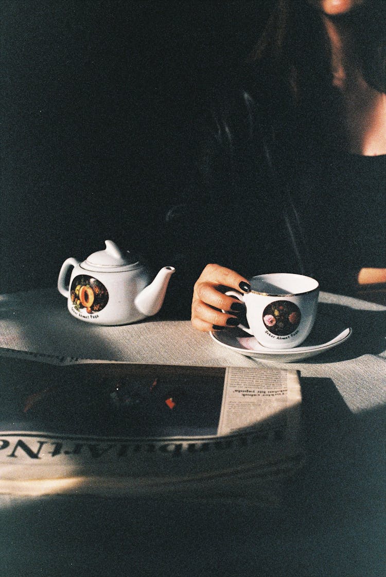 Woman Sitting At Table With Coffee And Newspaper In Shadow