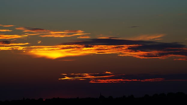 Breathtaking sunset with vivid orange and red clouds in a twilight sky over a silhouetted landscape.