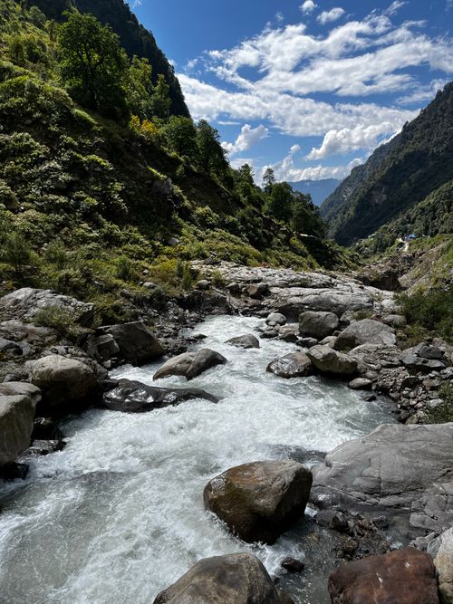 Free Mountain river cascading through a lush valley with clear blue skies and scenic forest views. Stock Photo