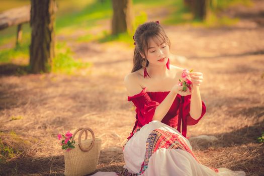 Young woman in a red dress sitting in a sunny park, enjoying a peaceful spring moment with flowers.