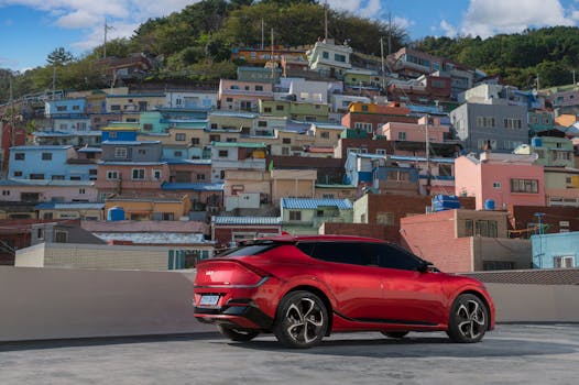 A sleek red car parked in front of colorful hillside houses in Busan, South Korea.