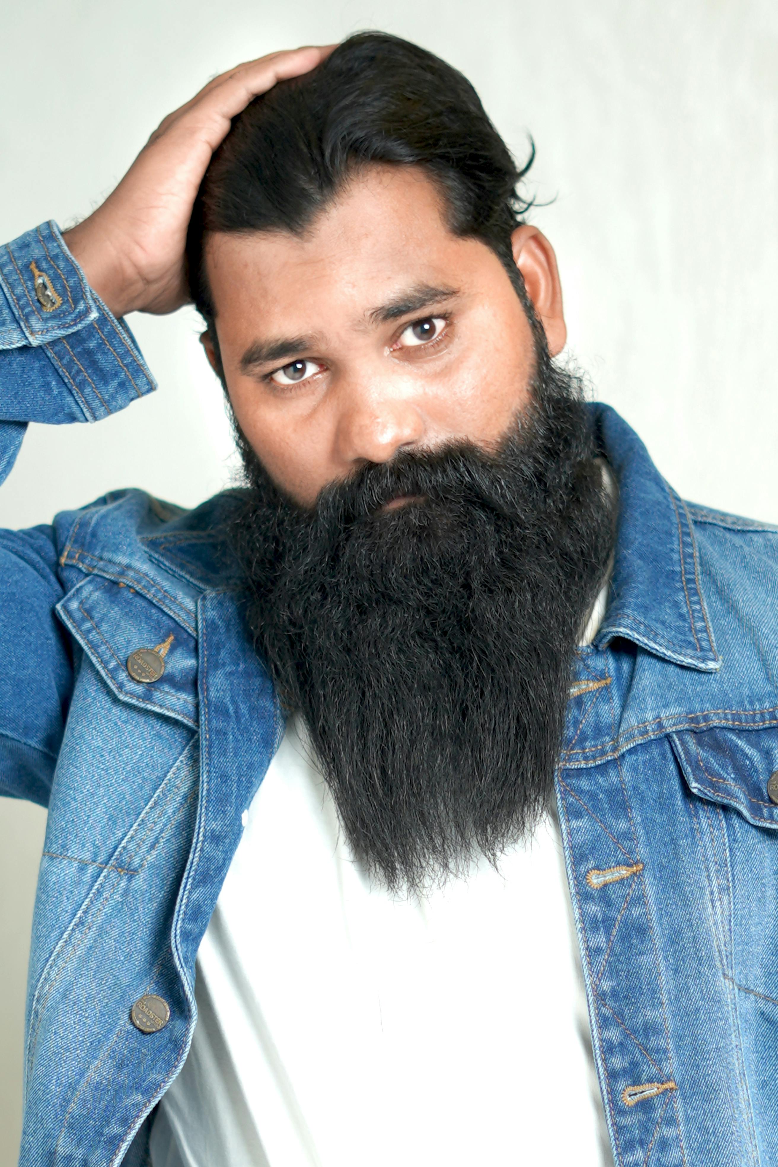 Bearded man wearing a denim jacket poses confidently in a studio setting.
