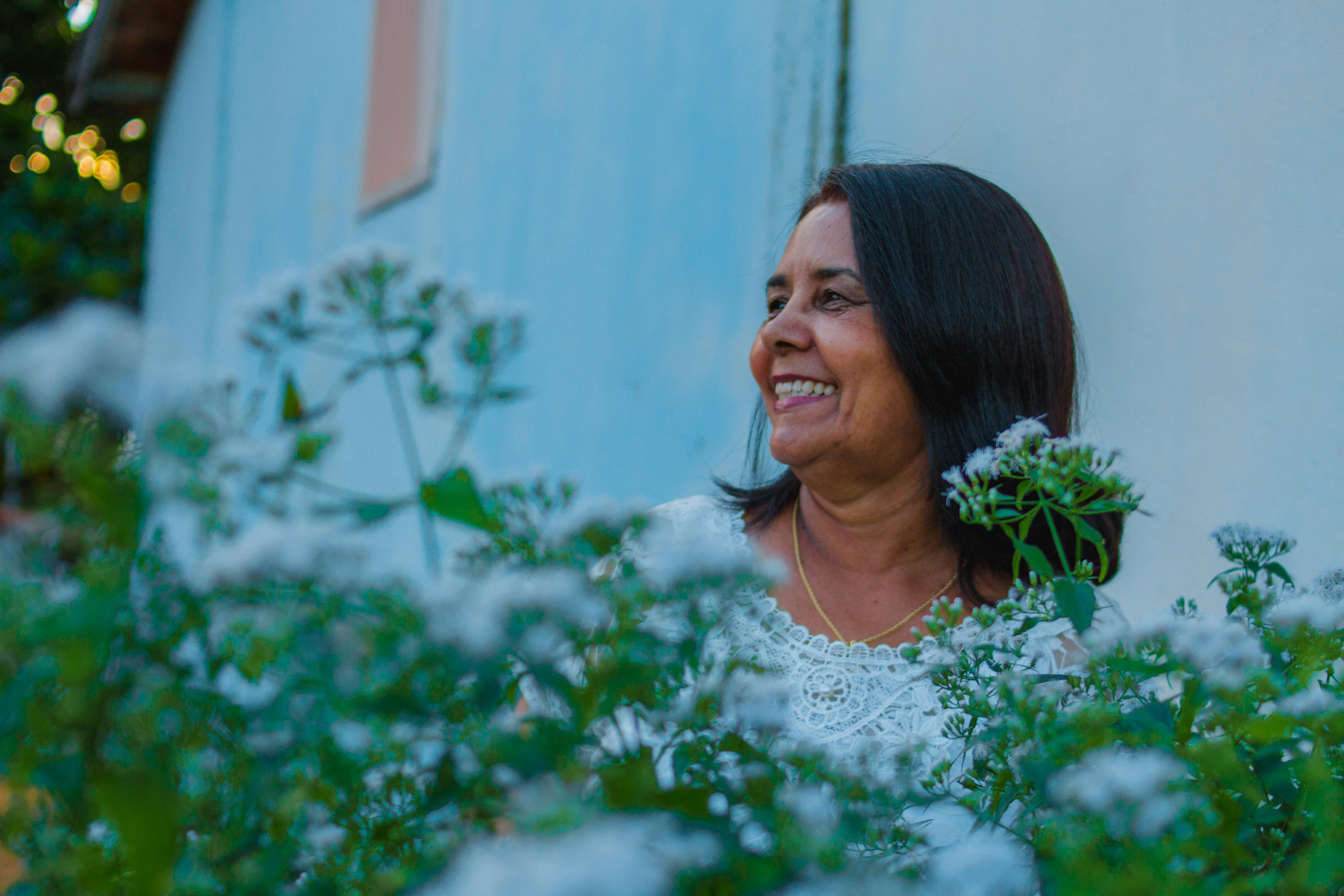 Joyful woman amidst white flowers, enjoying a bright day outdoors.