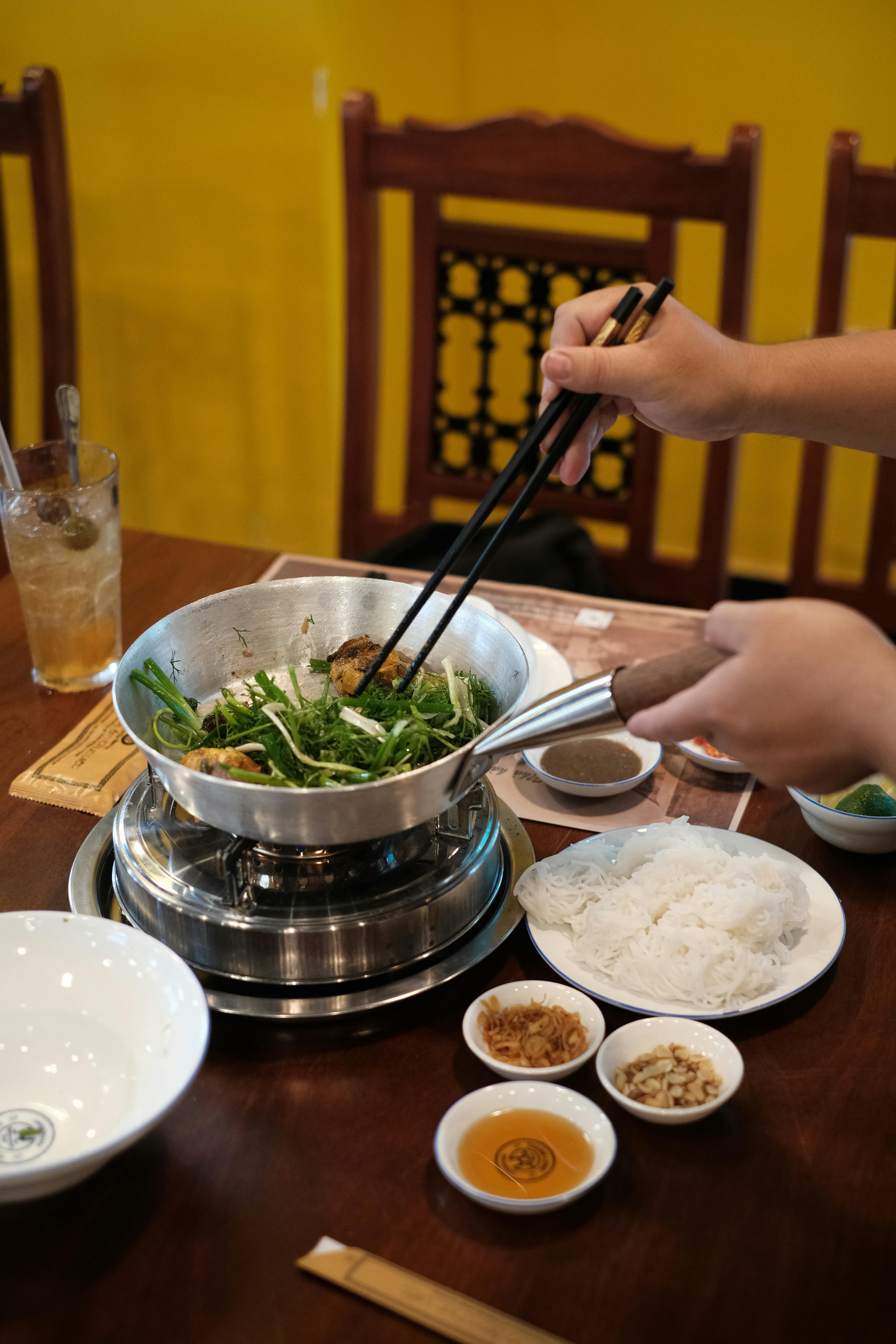 Close-up of a traditional Vietnamese meal being prepared at a wooden table, featuring fresh herbs and condiments.