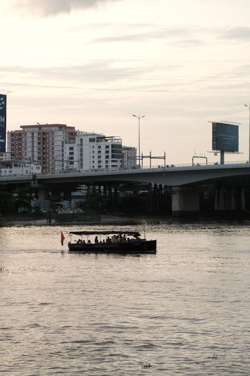 Free A boat travels beneath a city bridge on a calm river at dusk, capturing urban serenity. Stock Photo