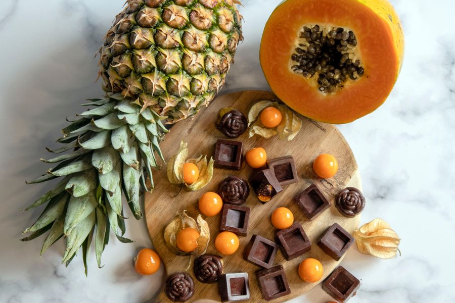 A vibrant arrangement of pineapple, papaya, and assorted chocolates on a wooden board and marble surface.
