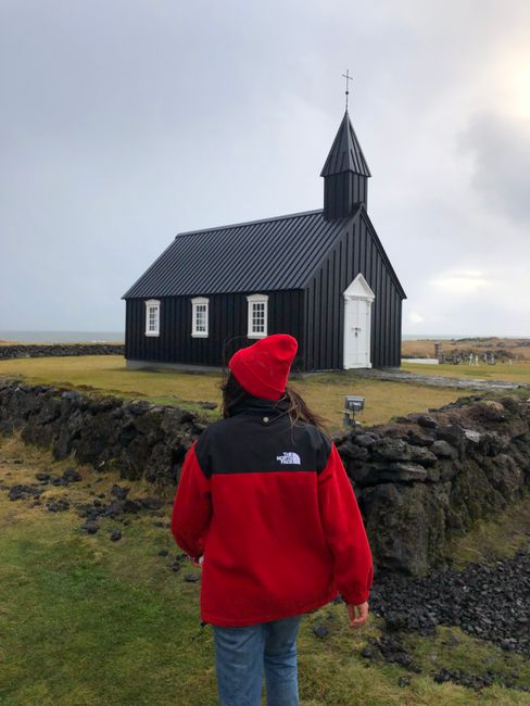 Person in red jacket approaches the iconic black church of Budir in Iceland.