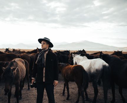 Man in cowboy hat among a herd of horses in a tranquil, open landscape.