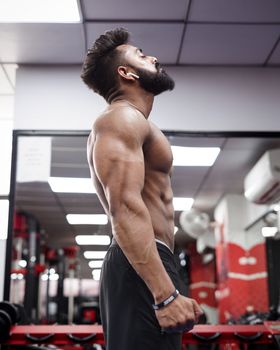 Side view of a muscular man in a gym environment showing strength and focus.