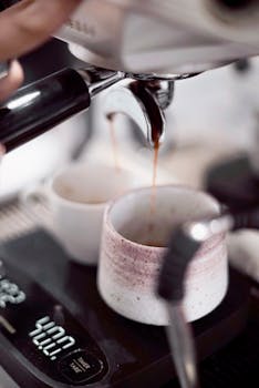 Detailed shot of coffee pouring into mugs from an espresso machine, showcasing barista technique.