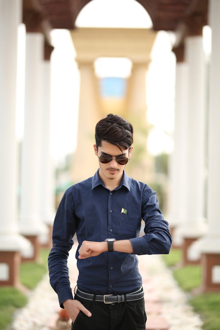 A Man In Blue Long Sleeves Wearing Sunglasses While Looking At The Time On His Watch