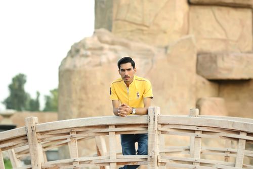 Free A young man in a yellow t-shirt stands on a wooden footbridge, looking directly at the camera. Stock Photo