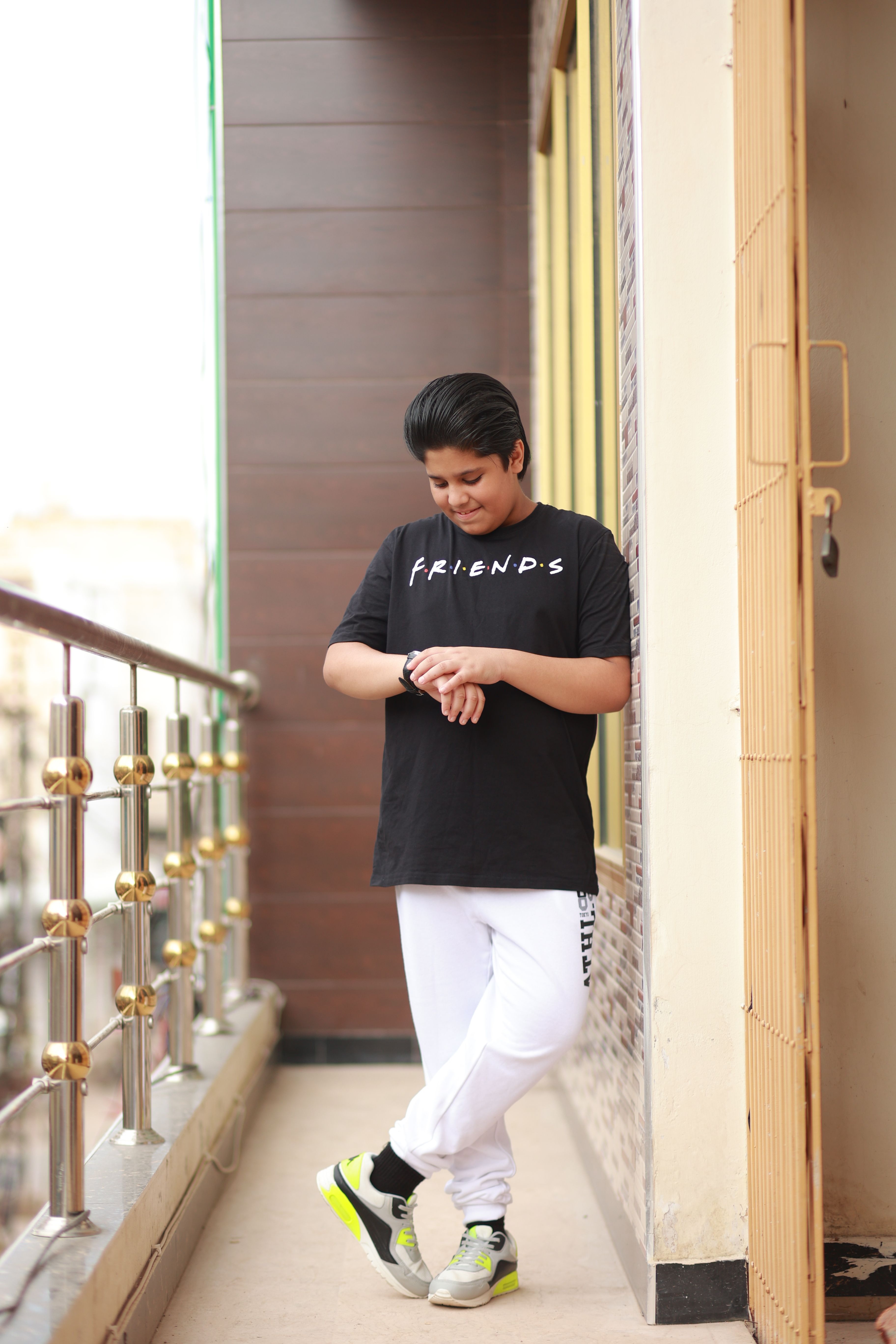 Casual teenager checking wristwatch on a modern apartment balcony wearing trendy outfit.