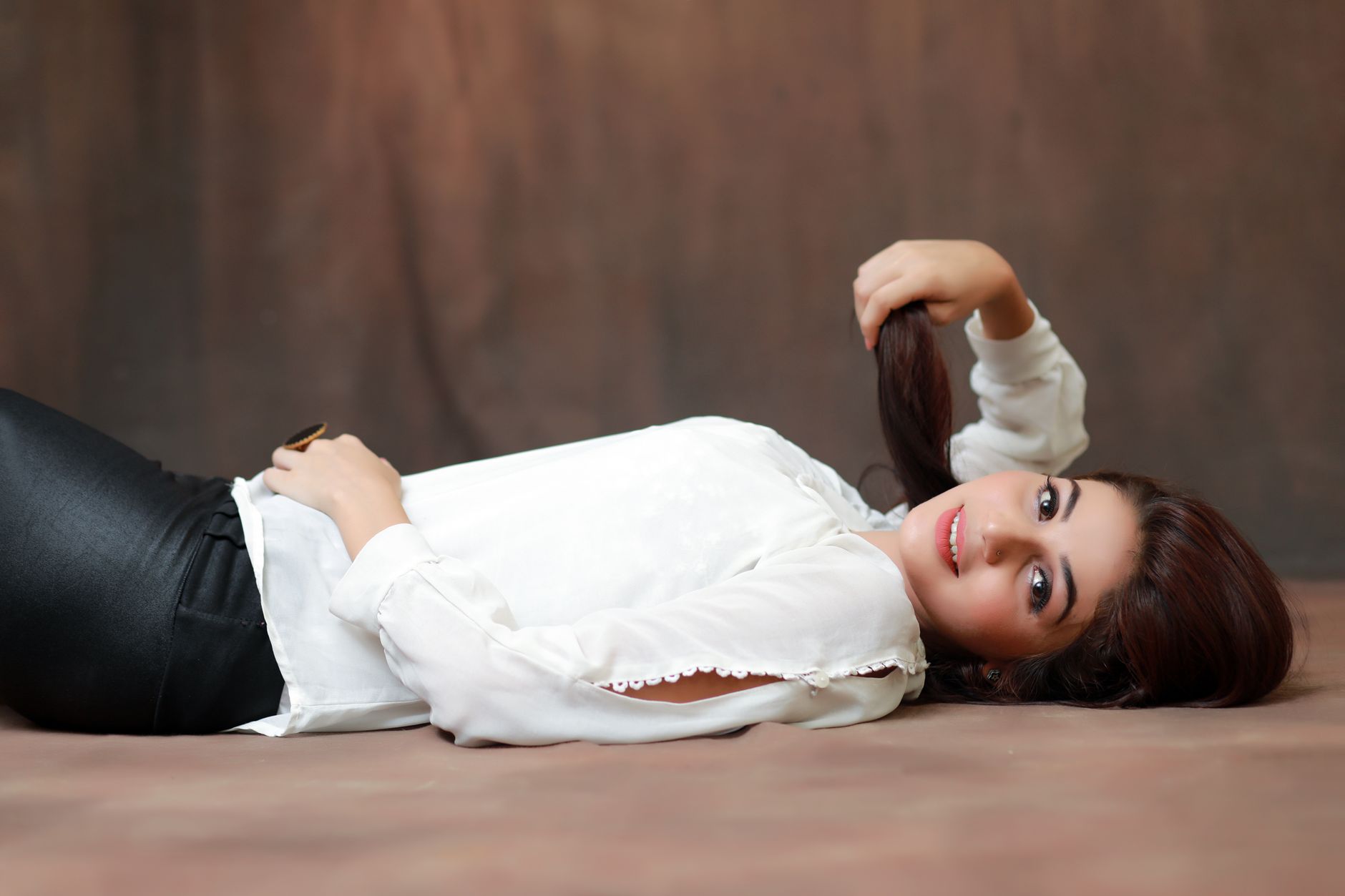 A woman lying on the floor in a stylish white blouse and black pants, smiling gracefully.