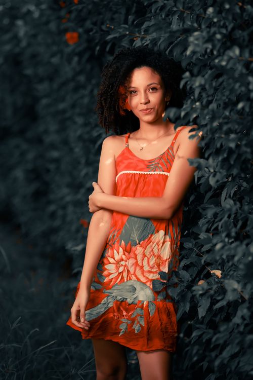 Free Smiling woman in a vibrant floral dress posing outdoors amidst lush green foliage. Stock Photo