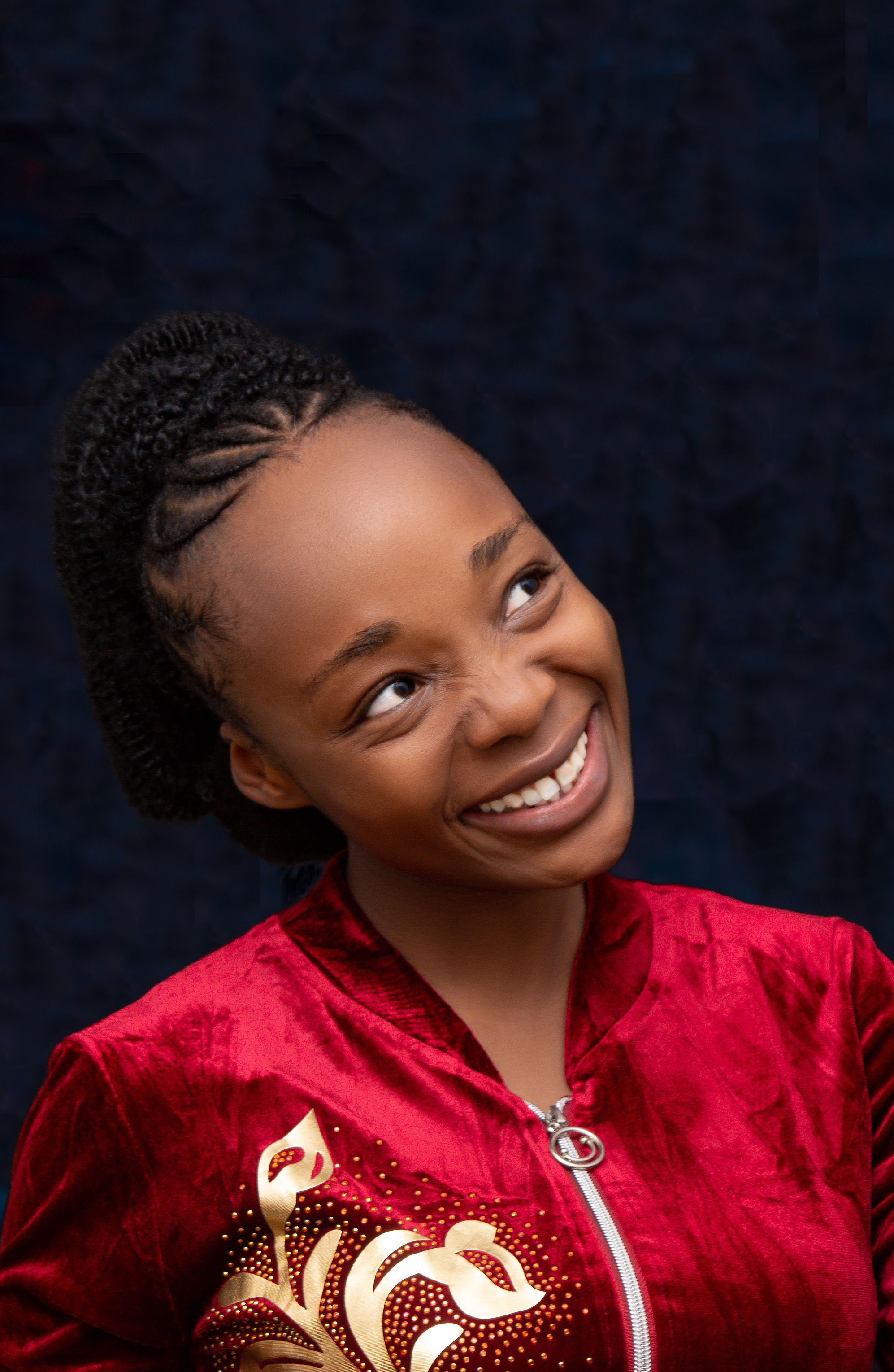 African American woman with braids smiling and looking upward in a vibrant red jacket.