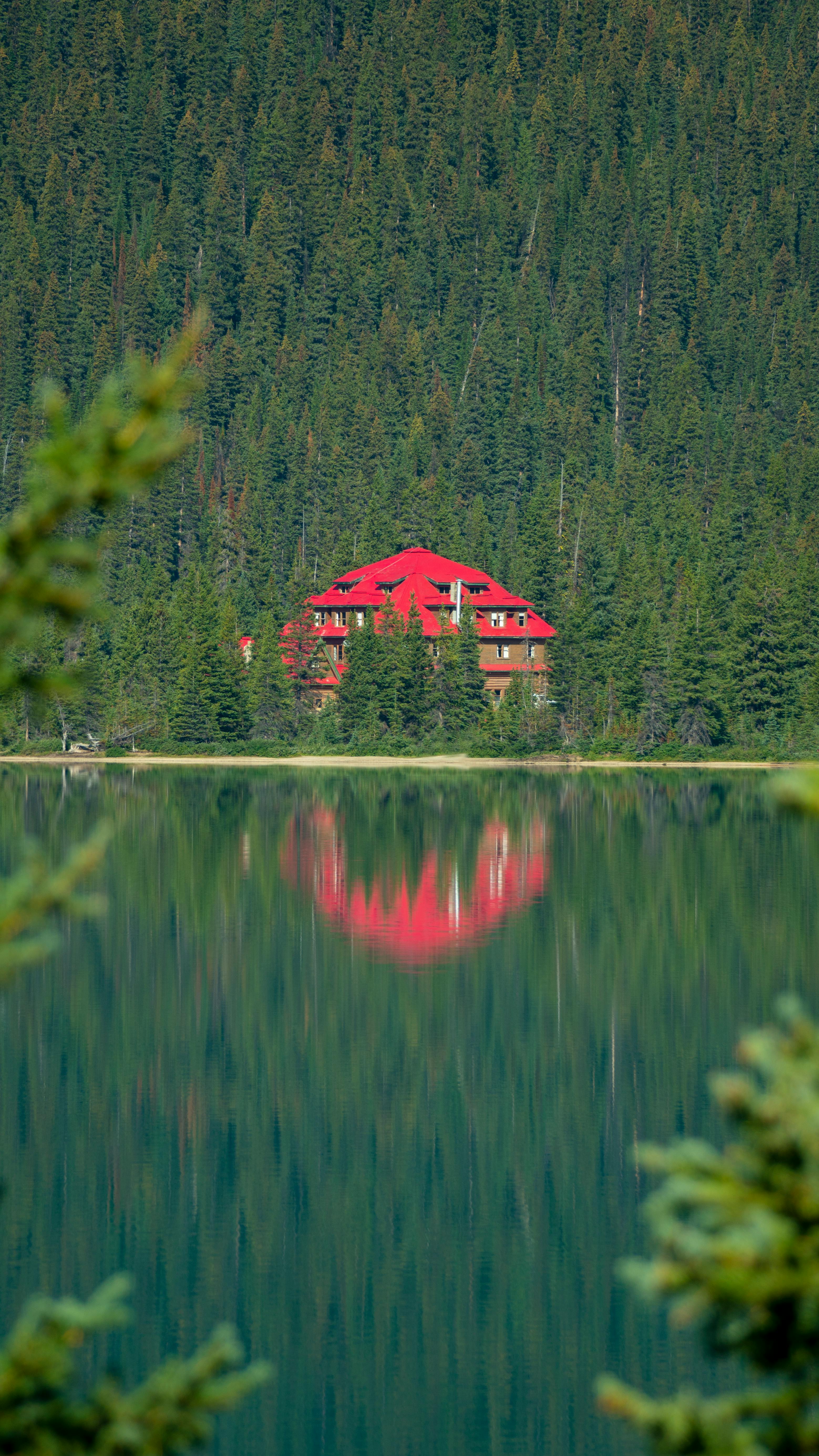 Red lodge reflecting in calm lake amid lush forest in Jasper, Alberta.