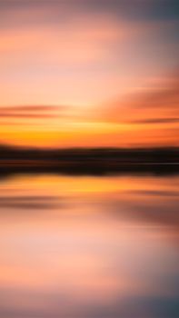 A peaceful sunset reflection on calm waters with vibrant orange and pink hues.