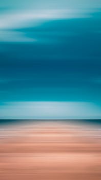 Blurred abstract beach with blue sky and sand, creating a serene visual effect.