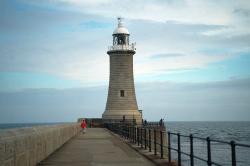 Free A serene view of a lighthouse standing tall on a pier, overlooking the calm ocean waters. Stock Photo