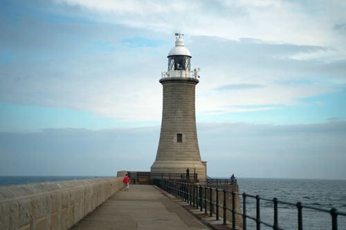 Free A lone lighthouse stands tall by the ocean under a cloudy sky, offering a serene coastal scene. Stock Photo