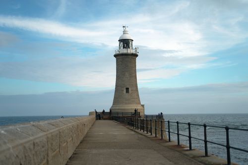 Free Scenic view of a lighthouse on a pier against a cloudy sky and ocean backdrop. Stock Photo