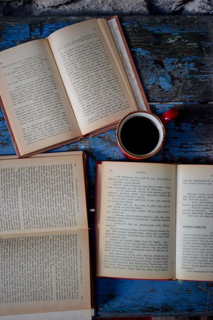 Open books and a red coffee cup on a rustic blue wooden table.