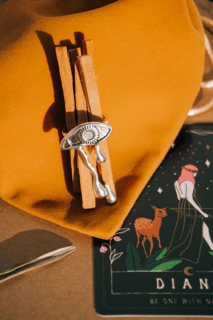 Close-up of cinnamon sticks with silver jewelry on yellow fabric next to a Diana tarot card.