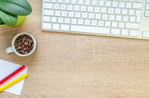 コーヒー豆と白いコーヒーマグの横にあるテーブルの上のシルバーアップルマジックキーボード