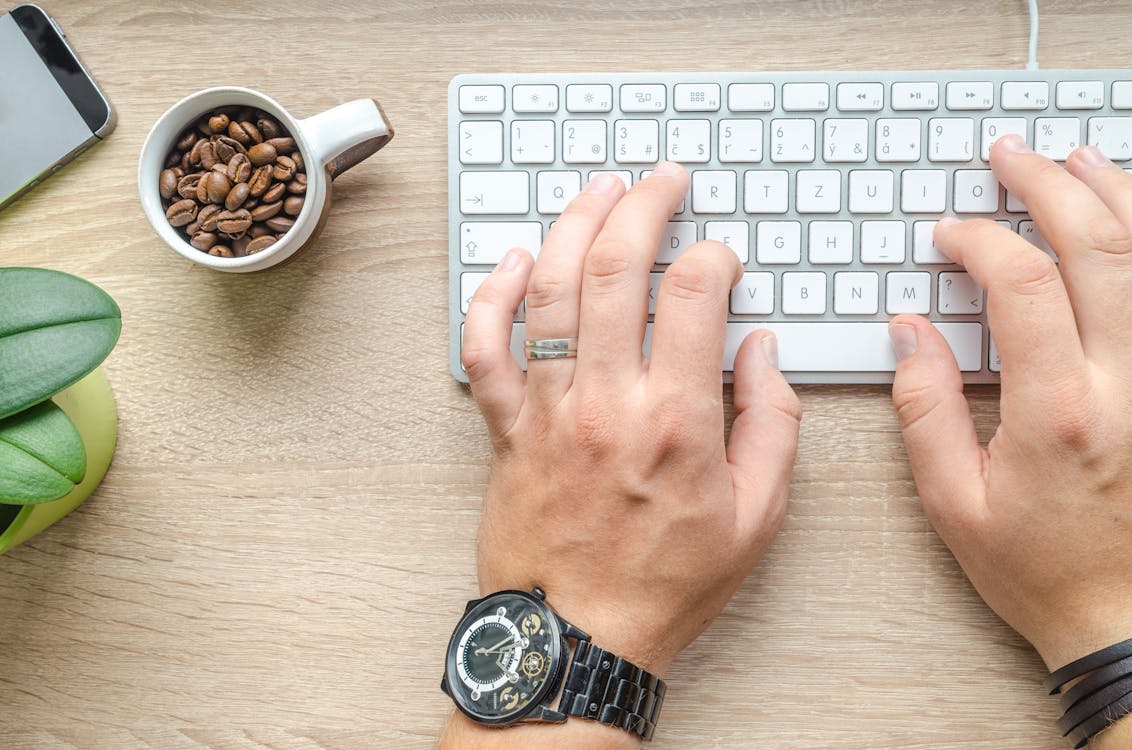 A person typing on a white keyboard next a cup of coffee beans.