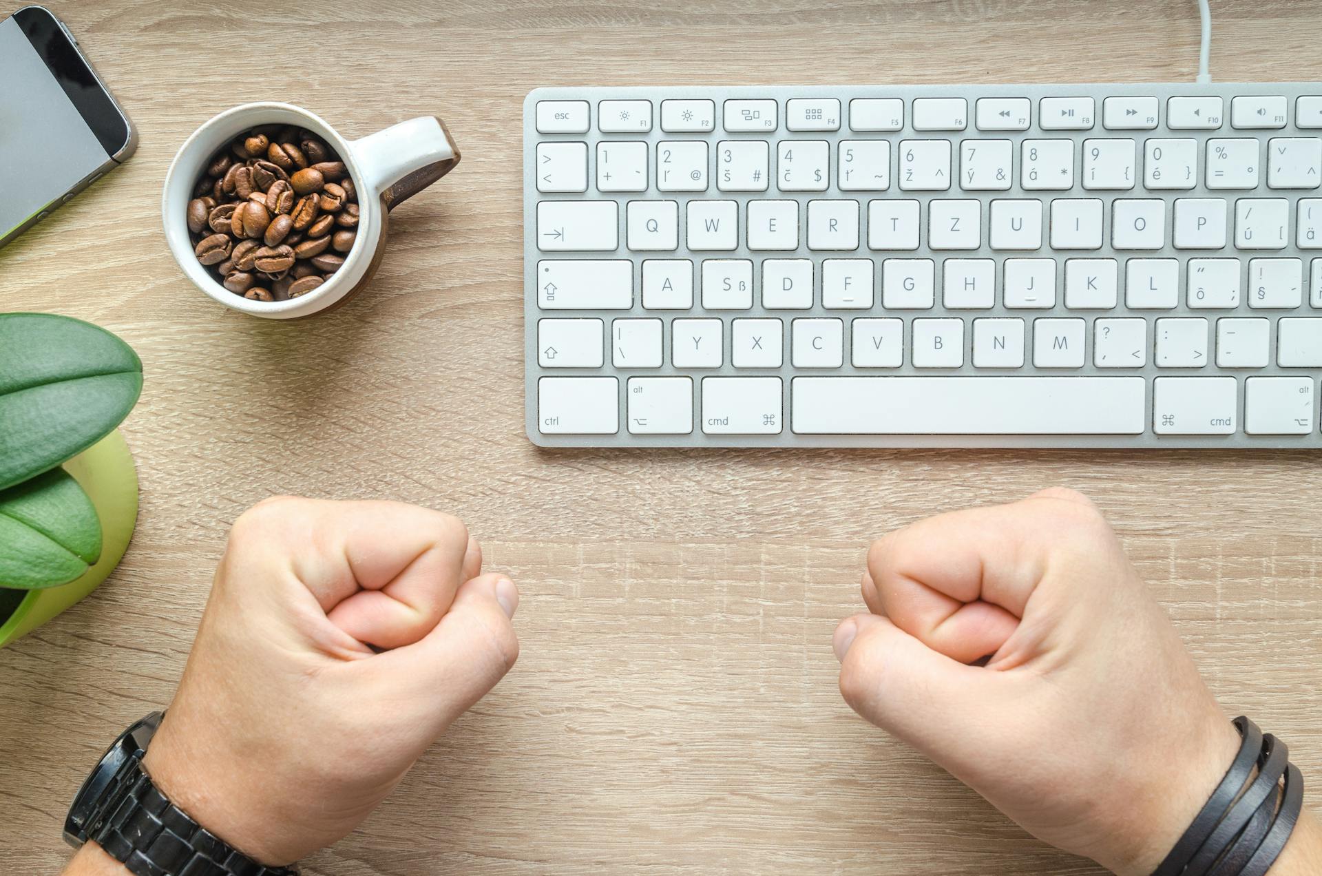 Top view of a desk with coffee beans cup, keyboard, plant, and fists. Ideal for business and technology themes.