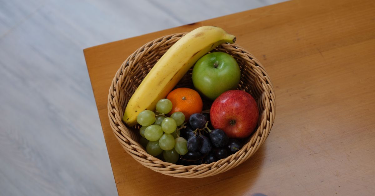 Variedade vibrante de frutas em uma cesta de vime sobre uma mesa de madeira.