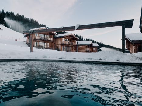 Idyllic wooden cabins by a lake in a snowy Italian village, showcasing winter beauty.
