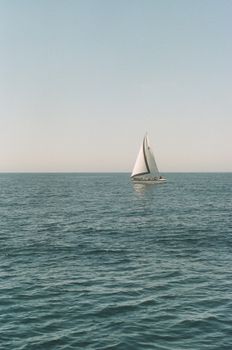 A lone sailboat sailing on a calm ocean under a clear sky near Long Beach, CA.