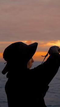 Captivating silhouette of a woman in black hat at sunset by the beach, capturing serene beauty.