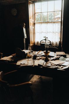 A dimly lit vintage study room filled with papers, antique furniture, and a window view.