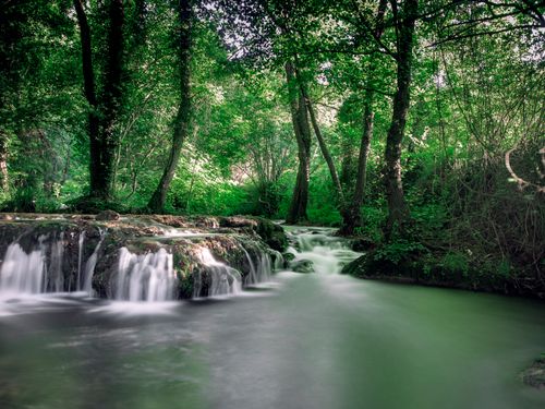 Free Serene long exposure of a cascading waterfall in a lush green forest setting. Stock Photo