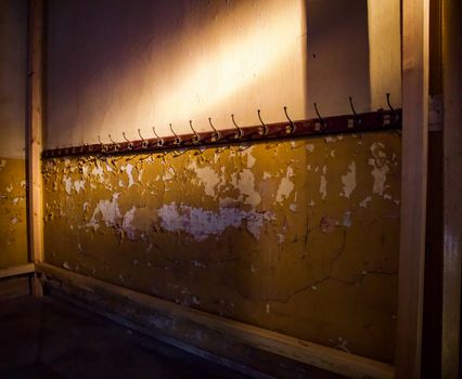 A dimly lit abandoned room with cracked yellow walls and coat hooks.