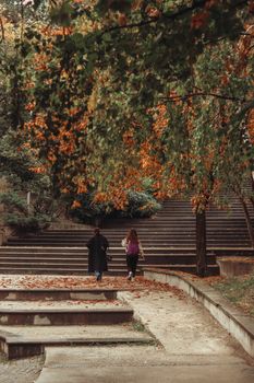 Two women walking in a scenic Ankara park during fall, surrounded by autumn leaves.