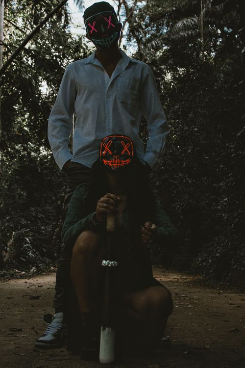 Free Two figures in neon masks stand and kneel on a forest path, creating a spooky atmosphere. Stock Photo