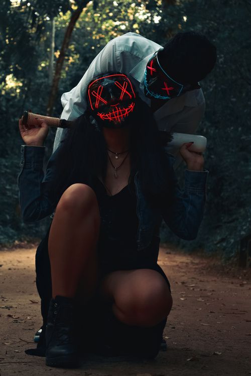 Free Two people wearing LED masks in a dark forest, creating a mysterious and eerie atmosphere. Stock Photo