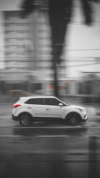 White SUV speeding through a rainy urban landscape, captured in blurred motion.