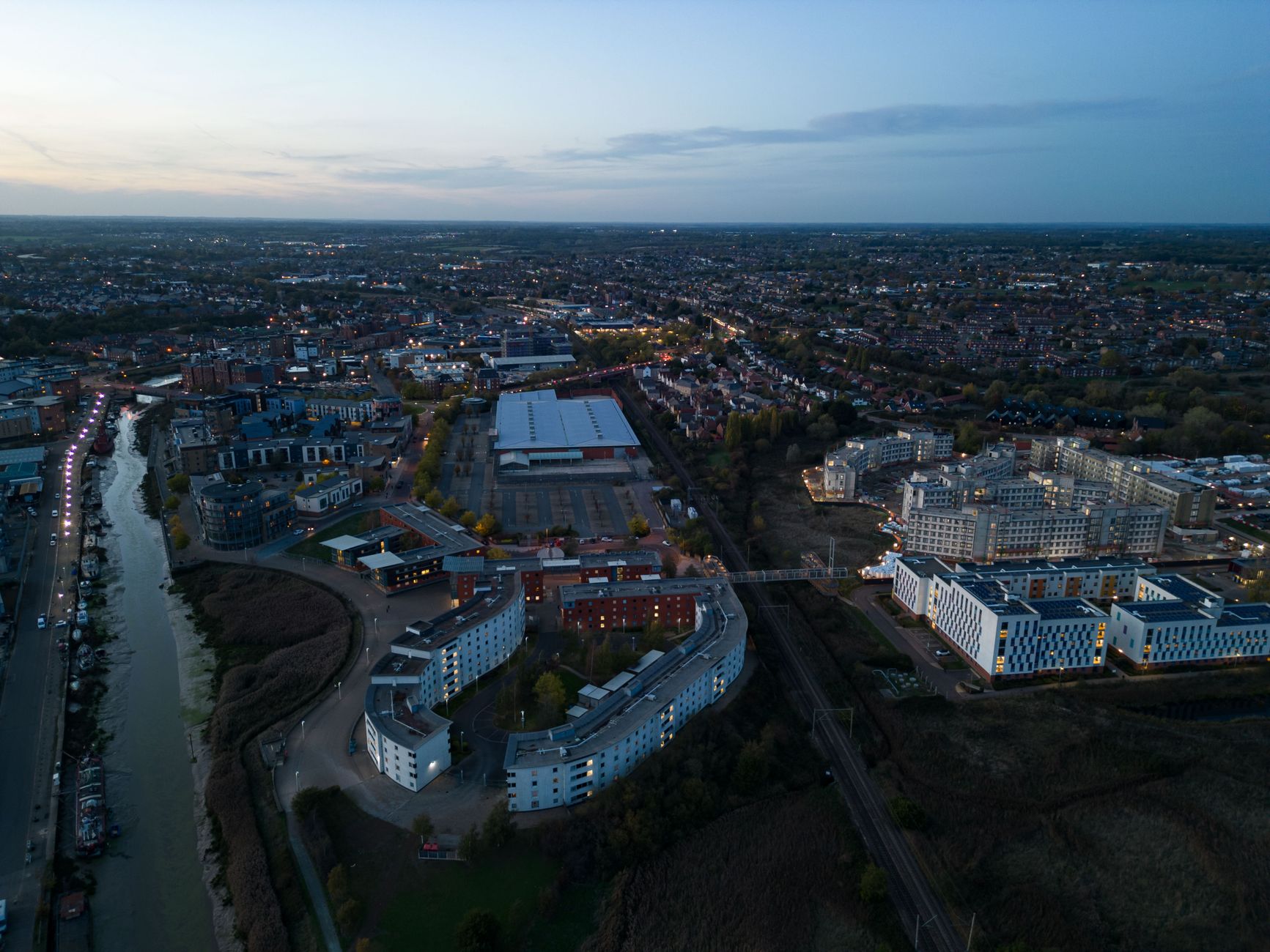 Aerial view of Colchester cityscape with river and buildings at dusk, showcasing urban landscape.