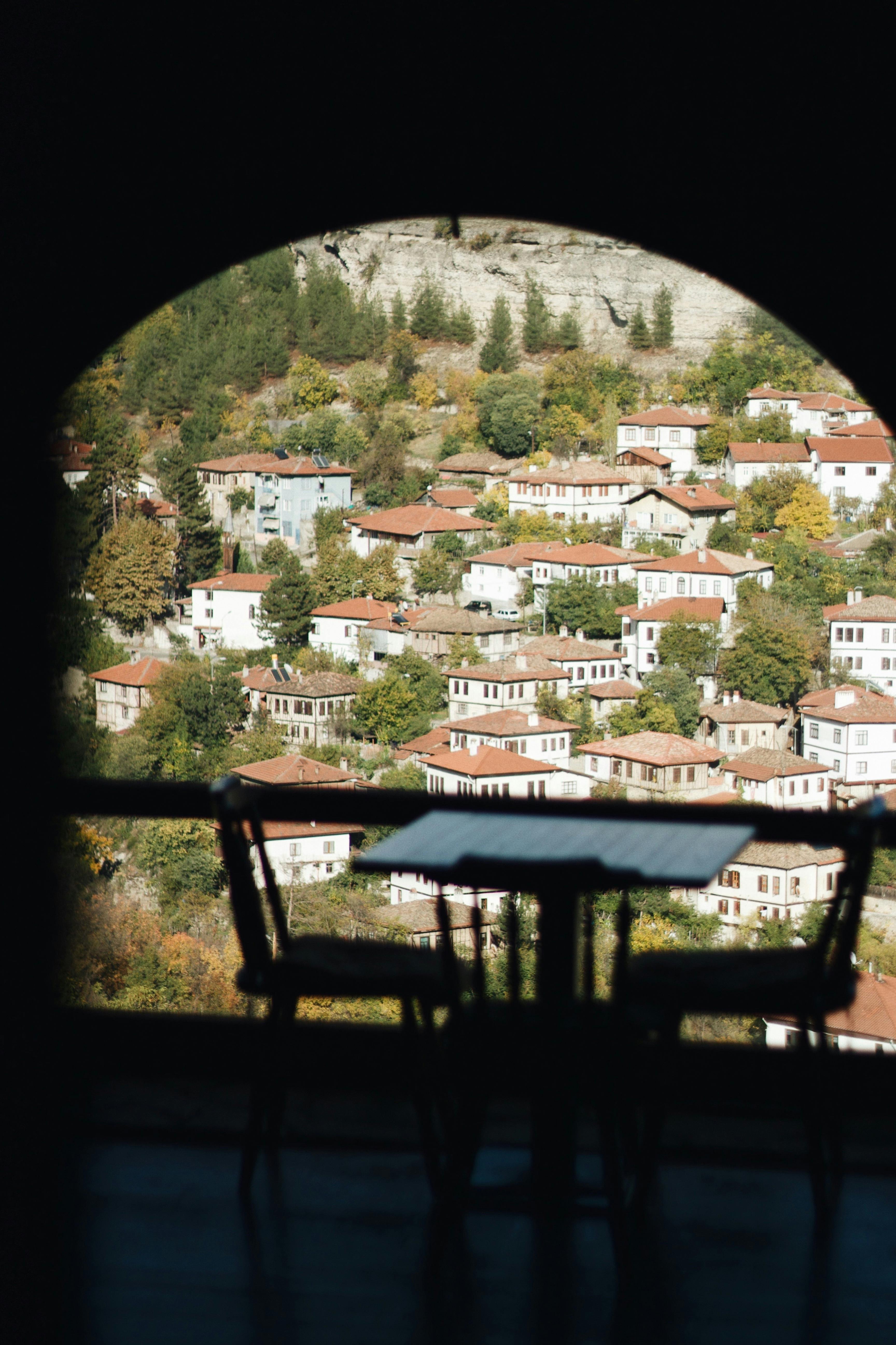 View of a picturesque hillside town through an arched balcony framing a table and chairs in silhouette.