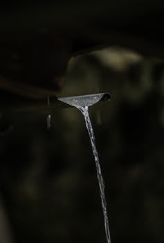 Close-up of rainwater pouring from a gutter, capturing the essence of nature