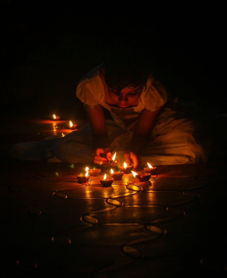 Girl Sitting On The Floor In The Dark And Lighting Candles 